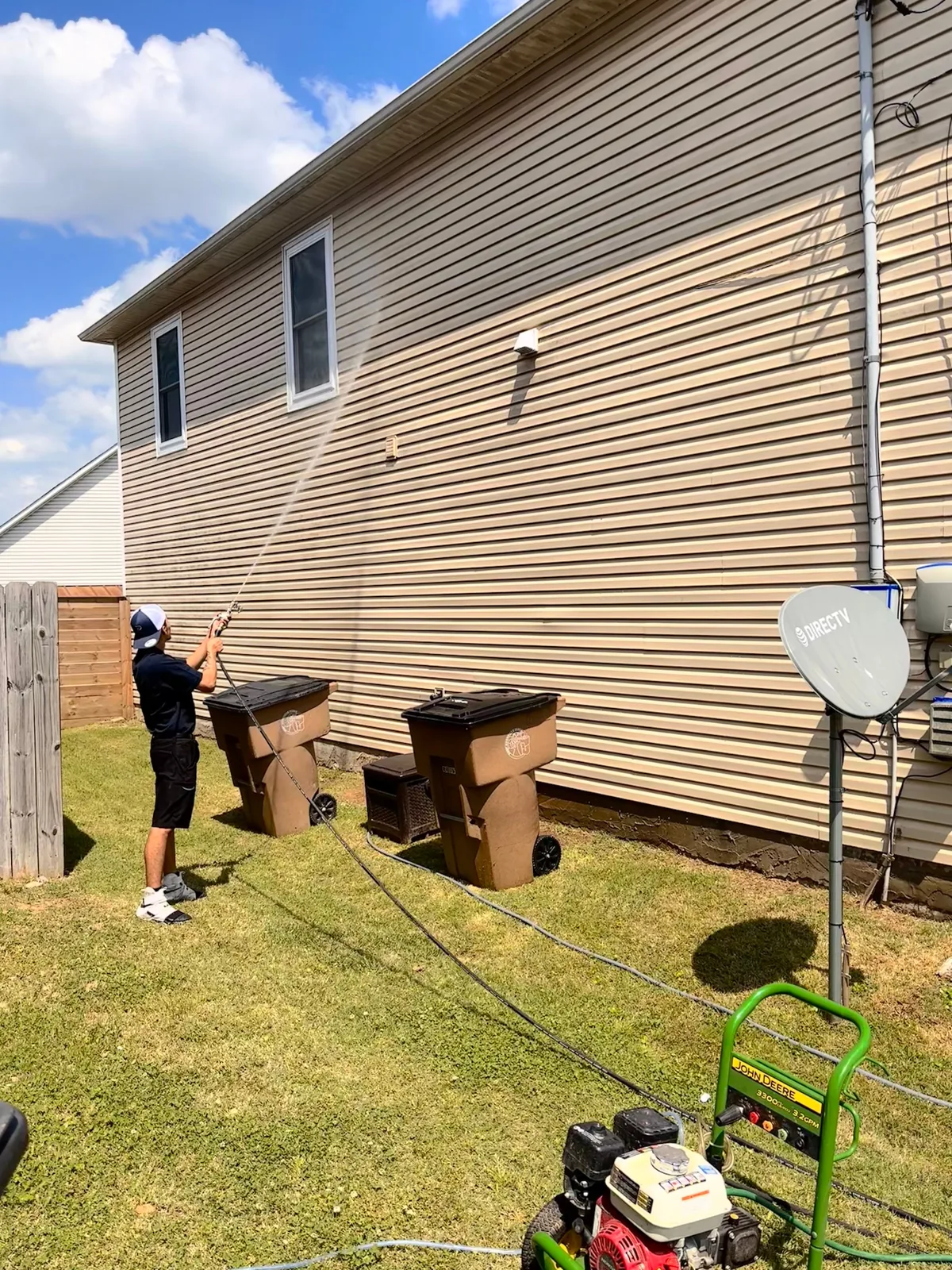 Drake soft washing the two-story vinyl siding of a house, pressure washer on the lawn